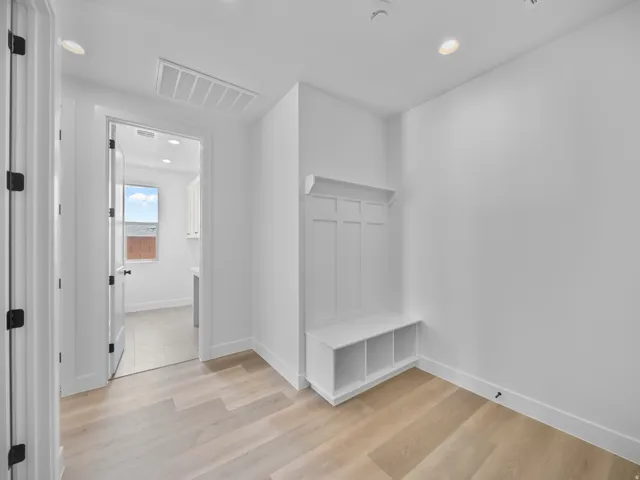 Light wood-finish flooring complemented by white walls, built-in coat rack, and recessed lighting