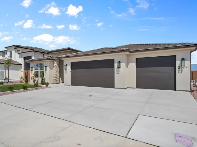 Stucco exterior with stone accents, two-car garage, concrete driveway, and front landscaping