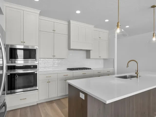 White cabinetry, stainless steel appliances, wood-finish flooring, white subway tile backsplash, and a kitchen island with an undermount sink