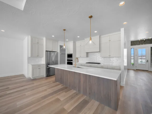Kitchen featuring a large island with wood-finish paneling, white shaker cabinetry, white subway tile backsplash, and stainless steel appliances