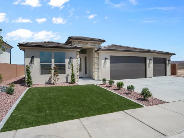 Stucco exterior with stone accents, dark tile roof, two-car garage, front yard with artificial turf and decorative rock landscaping, and a concrete driveway