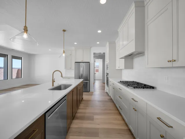 Expansive kitchen featuring a large island with an undermount sink, stainless steel appliances, light wood-finish flooring, white shaker cabinetry, and a gas range