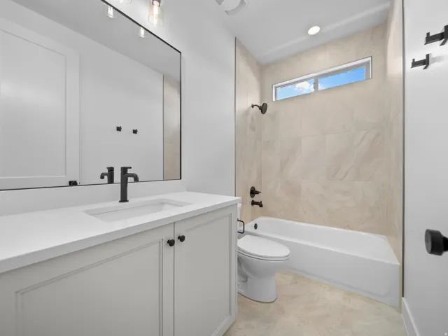 White vanity with integrated sink, black fixtures, and a frameless mirror