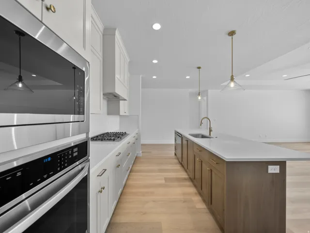 Contemporary kitchen featuring stainless steel appliances, white cabinetry, a gas cooktop, a large island with an undermount sink, and wood-finish flooring