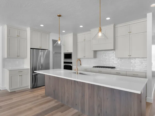 White shaker cabinetry, stainless steel appliances, wood-finish flooring, central island with seating, and pendant lighting