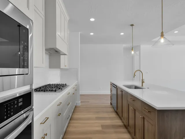 Kitchen featuring stainless steel appliances, a gas range with range hood, white cabinetry, wood-finish flooring, and an island with an undermount sink and brass faucet