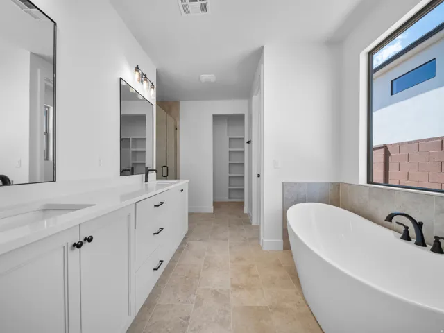 Dual vanity with quartz countertops, modern soaking tub, and tile flooring