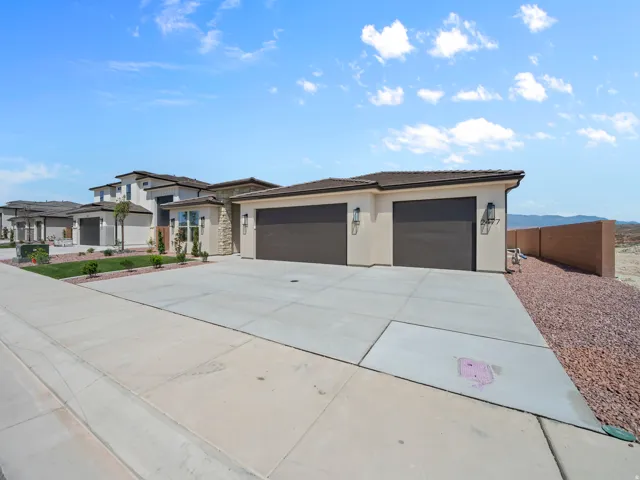 Stucco exterior featuring stone accents, a three-car garage, concrete driveway, and low-maintenance landscaping