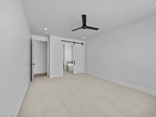 Plush carpeting, recessed lighting, matte black ceiling fan, and a modern barn door
