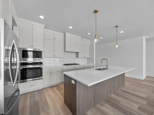 Gourmet kitchen with white shaker cabinetry, stainless steel appliances, subway tile backsplash, and a large center island with a built-in sink