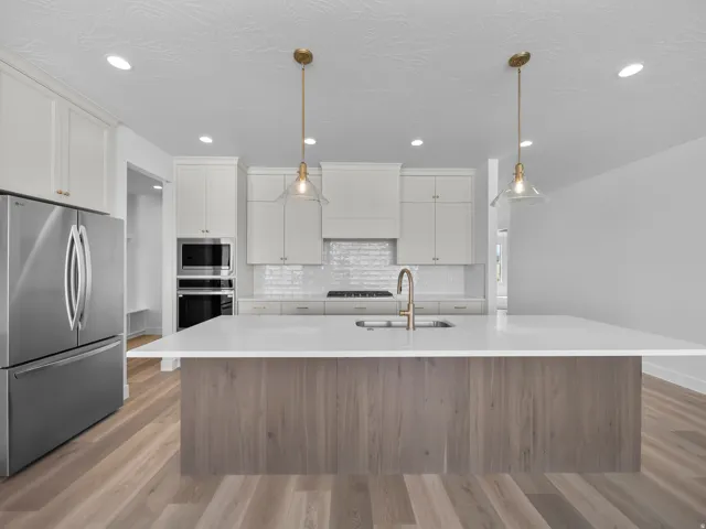 Kitchen featuring stainless steel appliances, white cabinetry, a large center island with a white countertop, wood-finish flooring, and pendant lighting