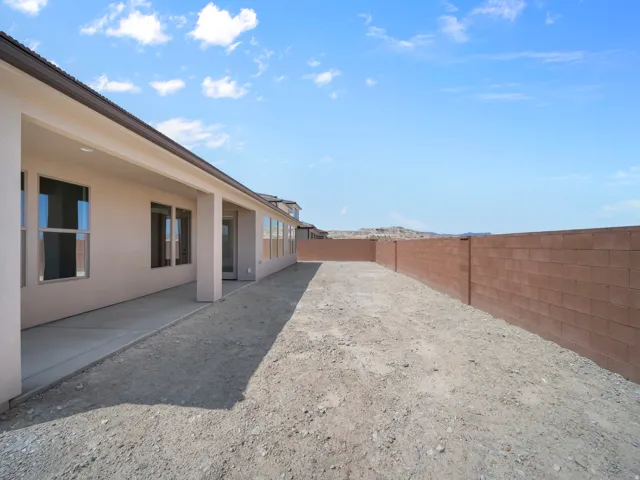 Expansive backyard with a covered patio, concrete slab, stucco exterior, multiple windows, and a block wall perimeter
