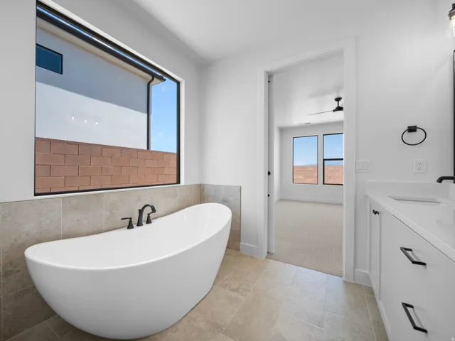 Freestanding soaking tub with a black faucet, large window, and tile flooring