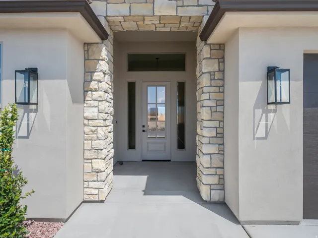 Stucco exterior with stone accents, covered entry, transom window, and modern exterior lighting fixtures