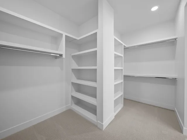 Built-in shelving, multiple hanging rods, recessed ceiling lighting, and neutral carpeting