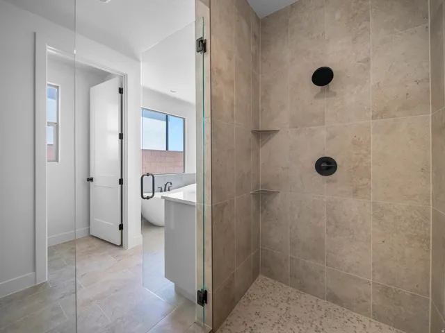 Walk-in shower with tiled walls and floor, matte black fixtures, and two corner shelves