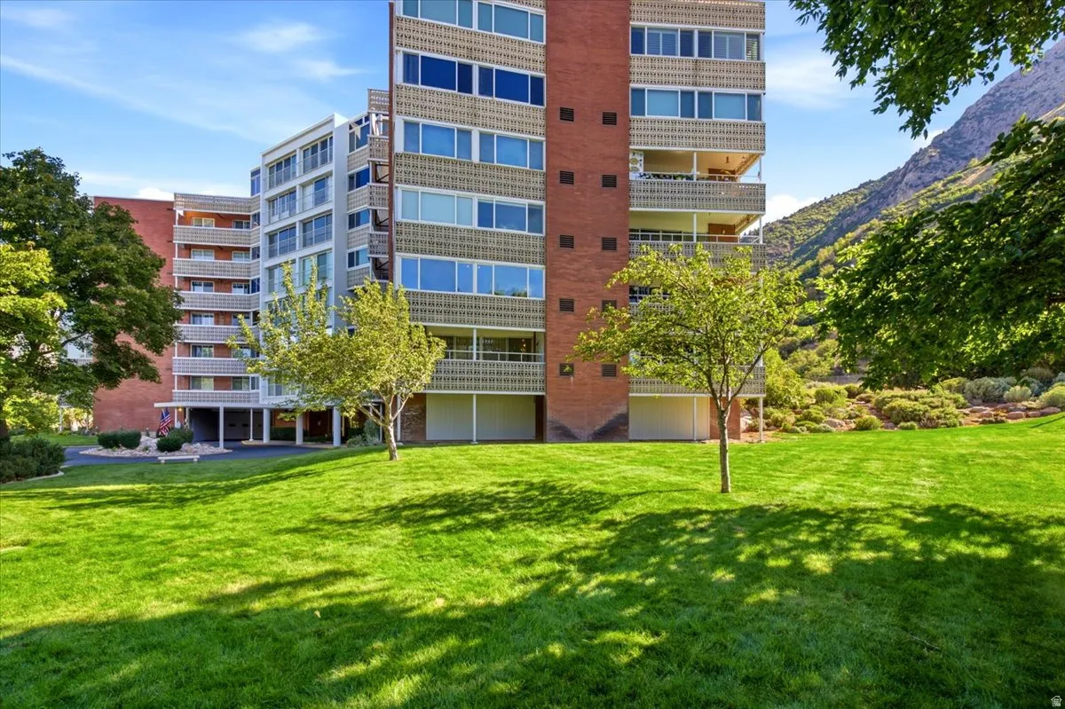 Expansive green lawn with mature trees, a multi-story building featuring brick and light-colored facades, and private balconies