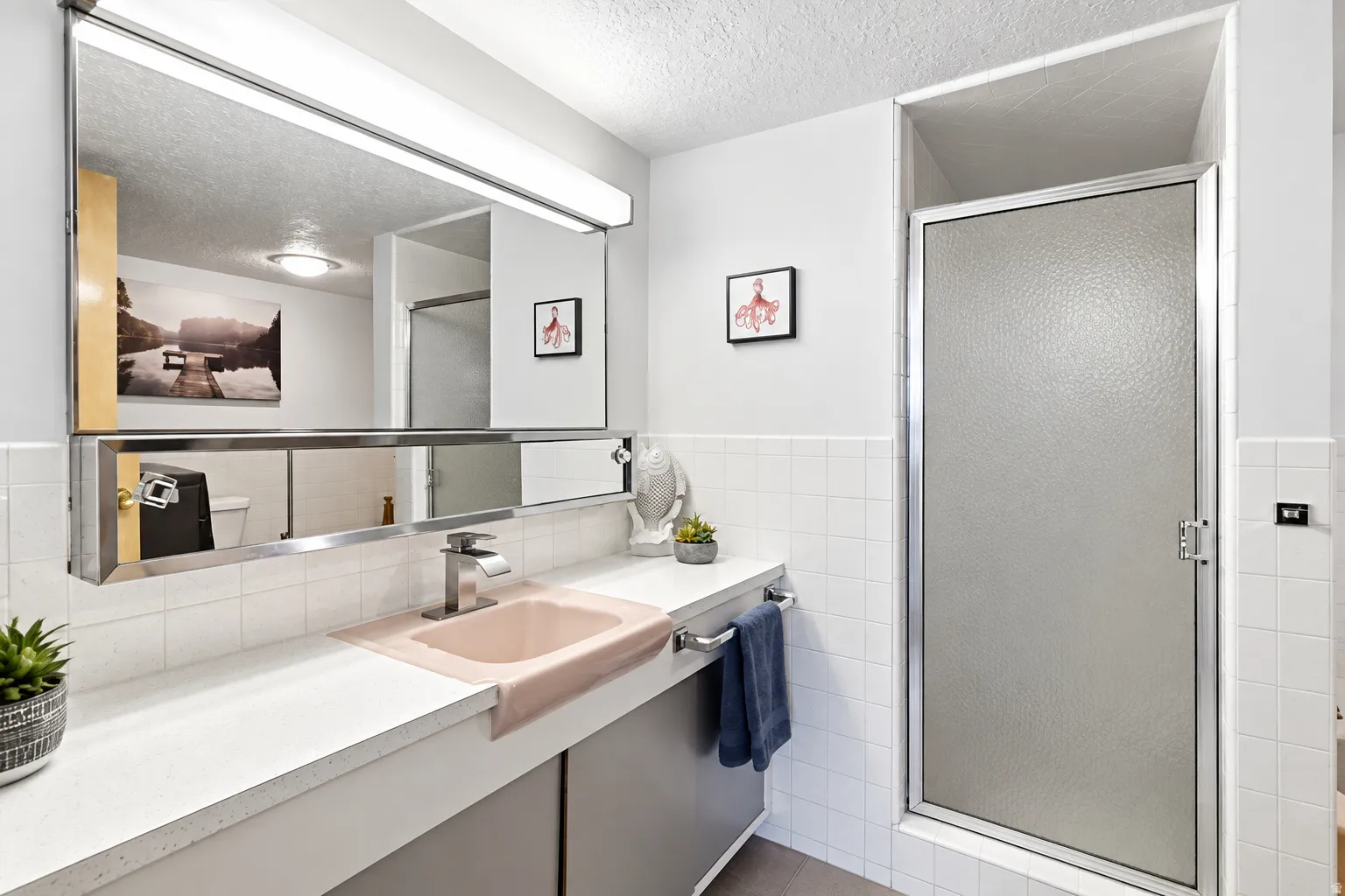 Vanity with integrated sink, expansive mirror, full-width vanity lighting, and a walk-in shower with textured glass door