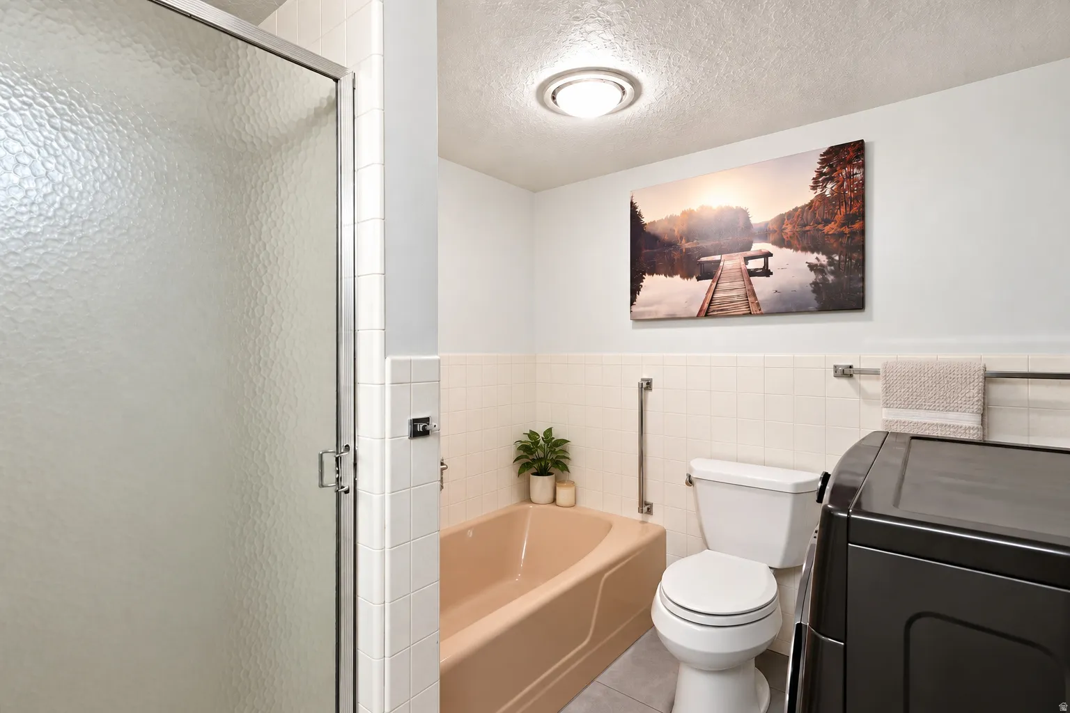 White tiled walls with a peach-toned bathtub and a shower enclosure featuring textured glass