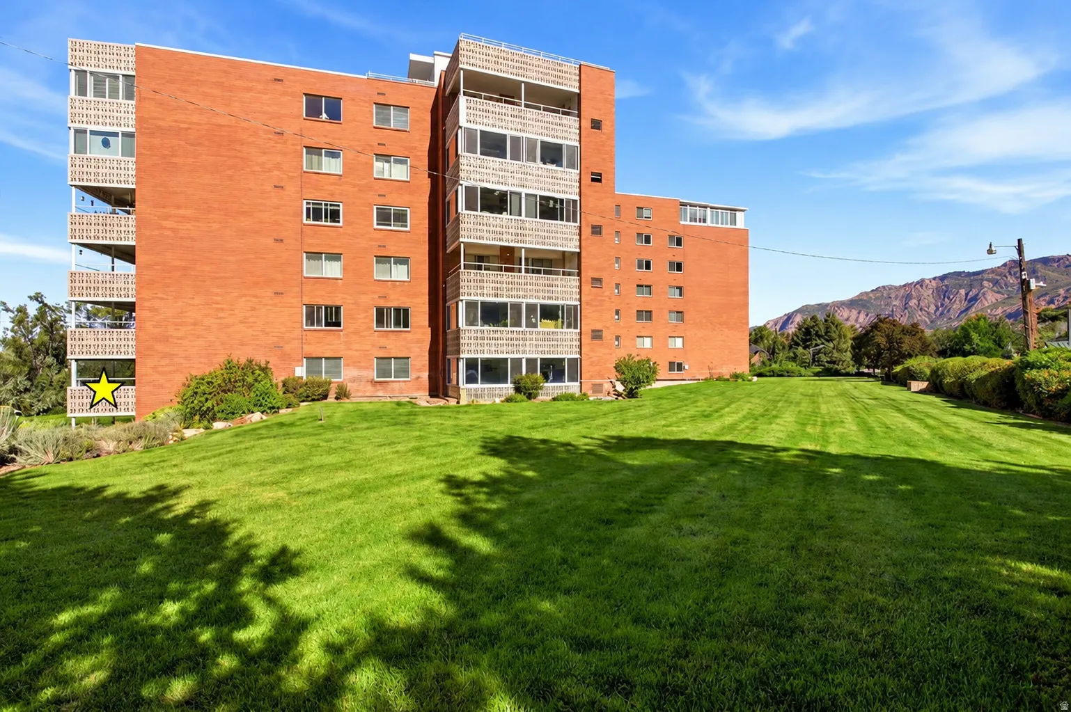 Brick exterior with multiple balconies, expansive green lawn, and distant mountains