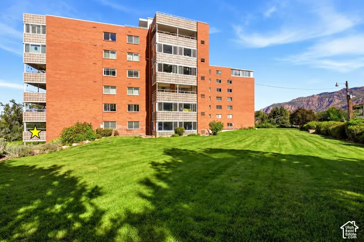Brick exterior with multiple balconies, expansive green lawn, and distant mountains