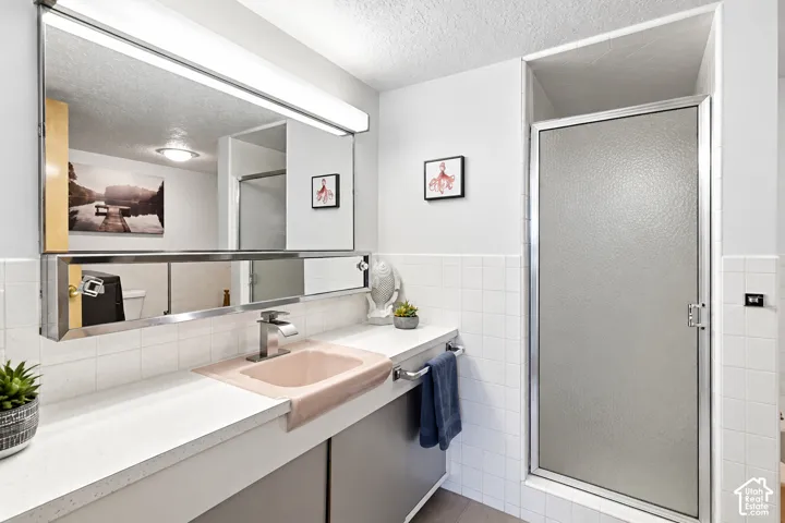 Vanity with integrated sink, expansive mirror, full-width vanity lighting, and a walk-in shower with textured glass door