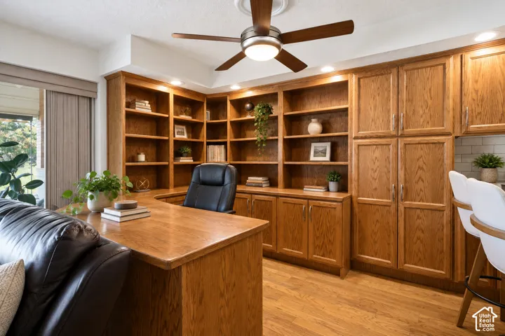 Built-in wood-finish shelving, wood-finish cabinetry, wood-finish flooring, recessed lighting, and a ceiling fan with integrated lighting