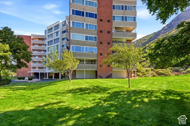 Expansive green lawn with mature trees, a multi-story building featuring brick and light-colored facades, and private balconies