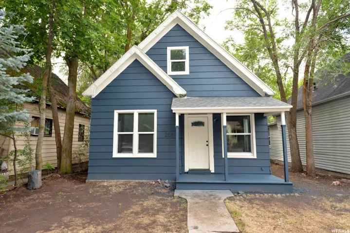 Gable roofline with white trim, blue siding exterior, covered porch, white entry door with upper glass panel, and multiple windows