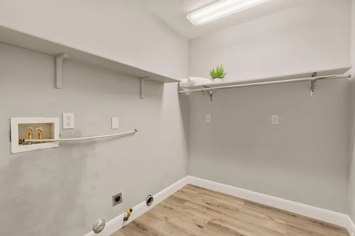Utility room featuring wood-finish flooring, two wall-mounted shelves, and a clothes hanging rod