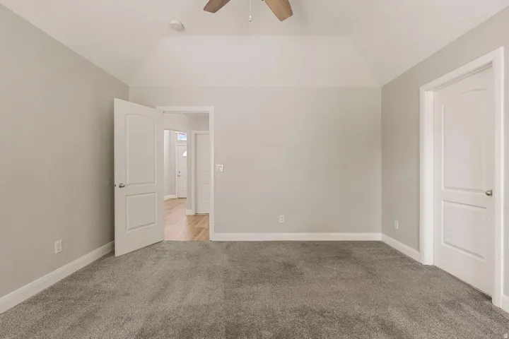 Vaulted ceiling, ceiling fan, neutral wall tones, gray carpet, and white trim