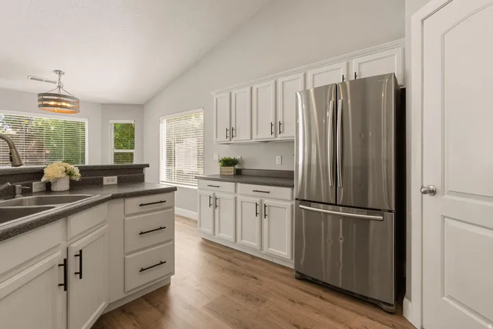 Kitchen featuring vaulted ceilings, white cabinetry, dark countertops, wood-finish flooring, and a stainless steel refrigerator