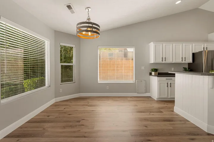 Vaulted ceilings, wood-finish flooring, white cabinetry with dark hardware, dark countertops, and a modern pendant light fixture