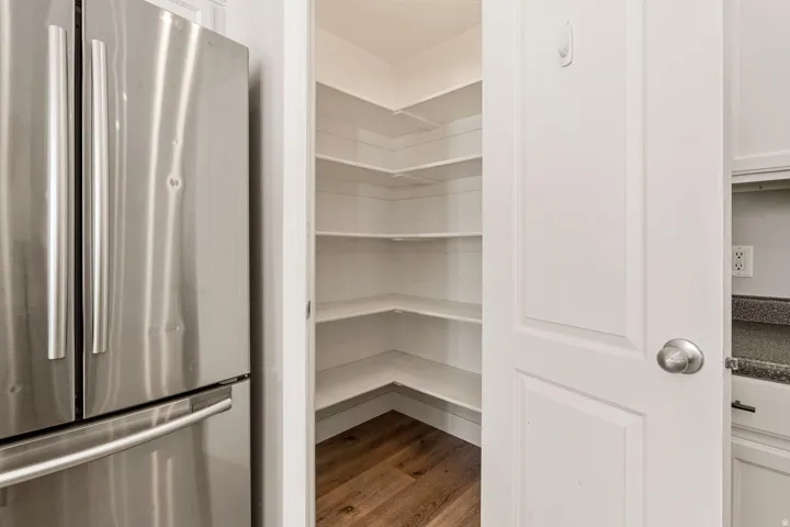 Walk-in pantry featuring built-in shelving, wood-finish flooring, and a paneled door