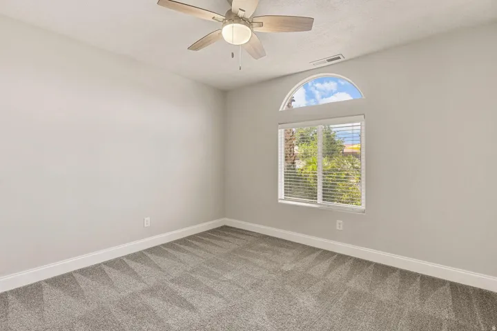 Room with an arched transom window, a standard window with blinds, a ceiling fan with light, and patterned gray carpeting