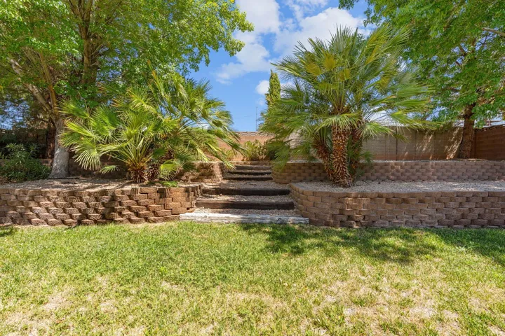 Terraced landscaping with interlocking block retaining walls, mature trees, and established palm trees