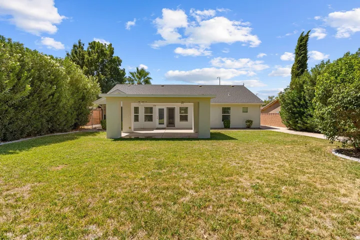 Expansive backyard featuring a covered patio, multiple glass panel doors, and mature perimeter landscaping