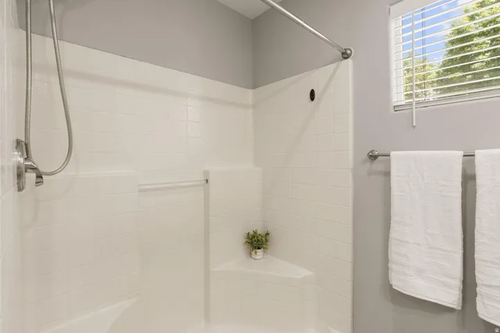 White subway tile surround, built-in shower seating, brushed metal shower fixtures, and a window with white blinds