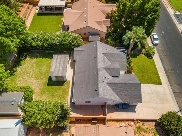 Shingled roof, mature landscaping, paved driveway, and a detached storage structure