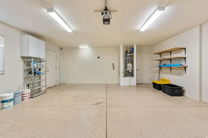 Spacious garage with bright overhead lighting, elevated cabinetry, built-in shelving, a dedicated water heater enclosure, and a textured concrete floor