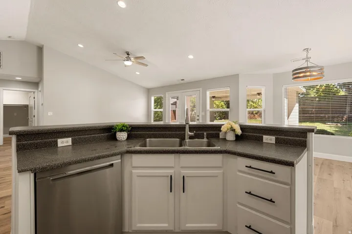 Kitchen featuring a double basin sink, stainless steel dishwasher, white cabinetry with dark hardware, and dark countertops