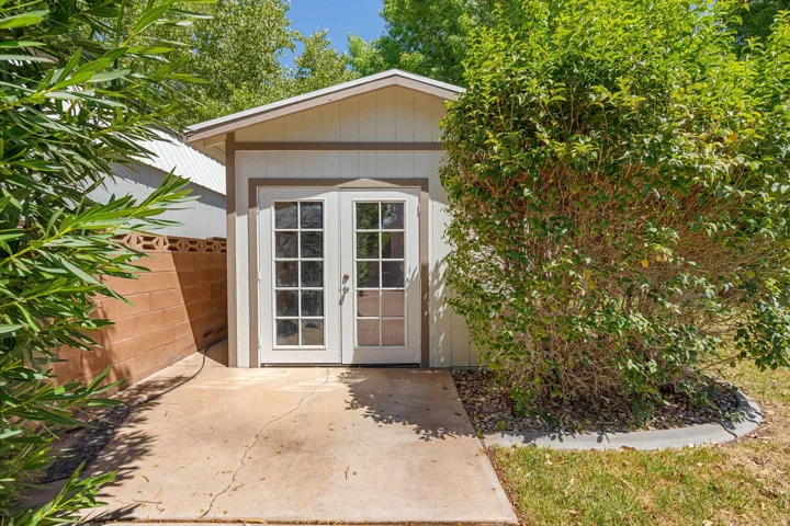 Detached structure with pitched roof, panel siding, double French doors, and concrete paver pathway