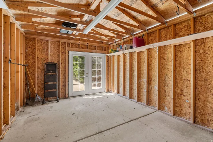 Concrete floor, exposed wood framing, built-in shelving, fluorescent overhead lighting, and double French doors