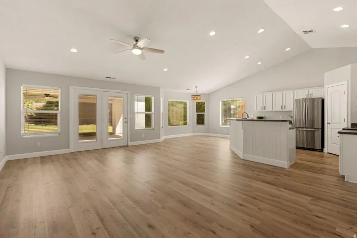 Vaulted ceiling with recessed lighting, wood-finish flooring, white shaker cabinetry, stainless steel refrigerator, and glass-paneled double doors
