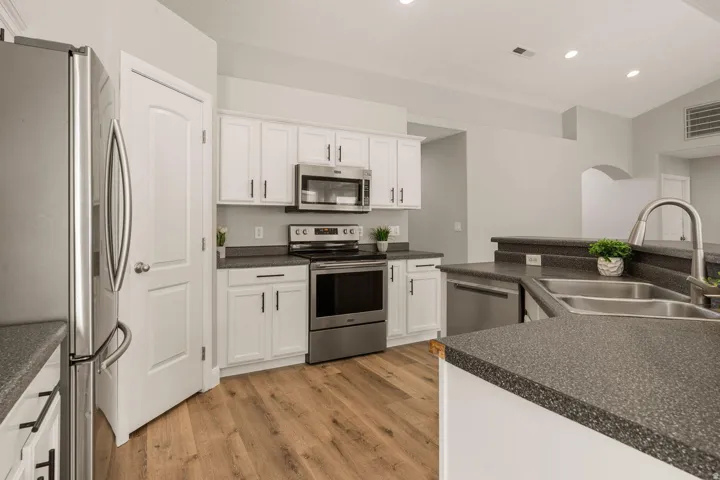 Kitchen featuring white cabinetry, dark speckled countertops, stainless steel appliances, wood-finish flooring, and a double basin sink