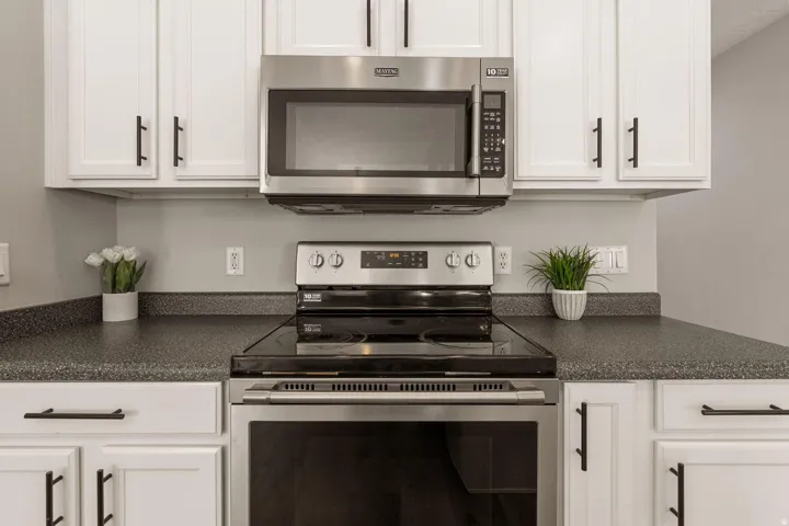 White shaker-style cabinetry with matte black hardware, stainless steel microwave, black electric range, and dark speckled countertops