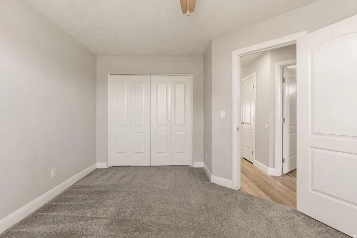 Neutral gray wall paint, textured ceiling, light gray carpet flooring, white bi-fold closet doors, white interior doors
