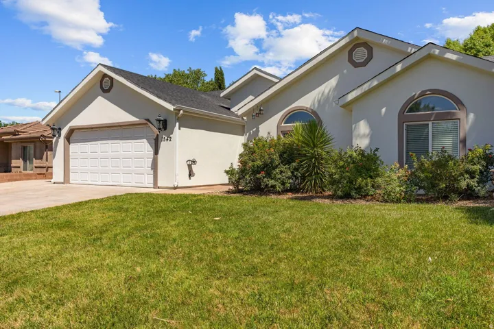 Stucco exterior with arched windows, prominent gables, an attached garage, and mature landscaping