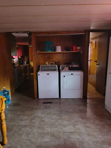 Laundry area featuring wood-finish paneling, an overhead shelf, and tile-look flooring