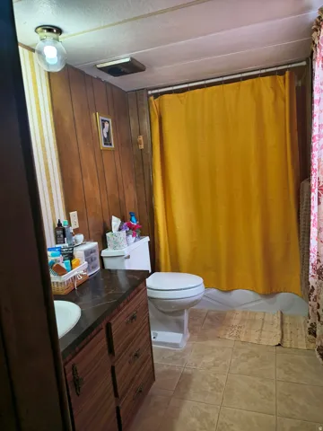 Wood-paneled wall, built-in vanity with dark countertop, white drop-in sink, and ceramic tile flooring